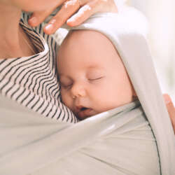 Babywearing. Mother and baby on nature outdoors. Baby in wrap carrier. Woman carrying little child in baby sling in green mint color. Concept of green parenting, natural motherhood, postpartum period.