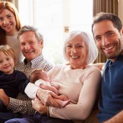 Multi Generation Family Sitting On Sofa With Newborn Baby